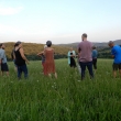 Gruppe von Männern und Frauen im Kreis stehend in hohem Gras mit Hügeln im Hintergrund