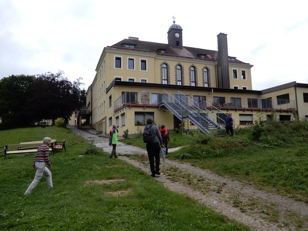 WanderInnen auf einem Schotterweg vor den Gebäuden des Projektes LebensGut Miteinander