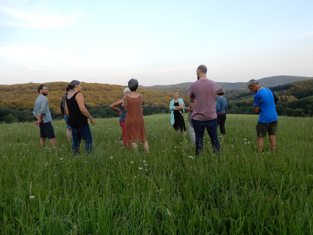 Gruppe von Männern und Frauen im Kreis stehend in hohem Gras mit Hügeln im Hintergrund