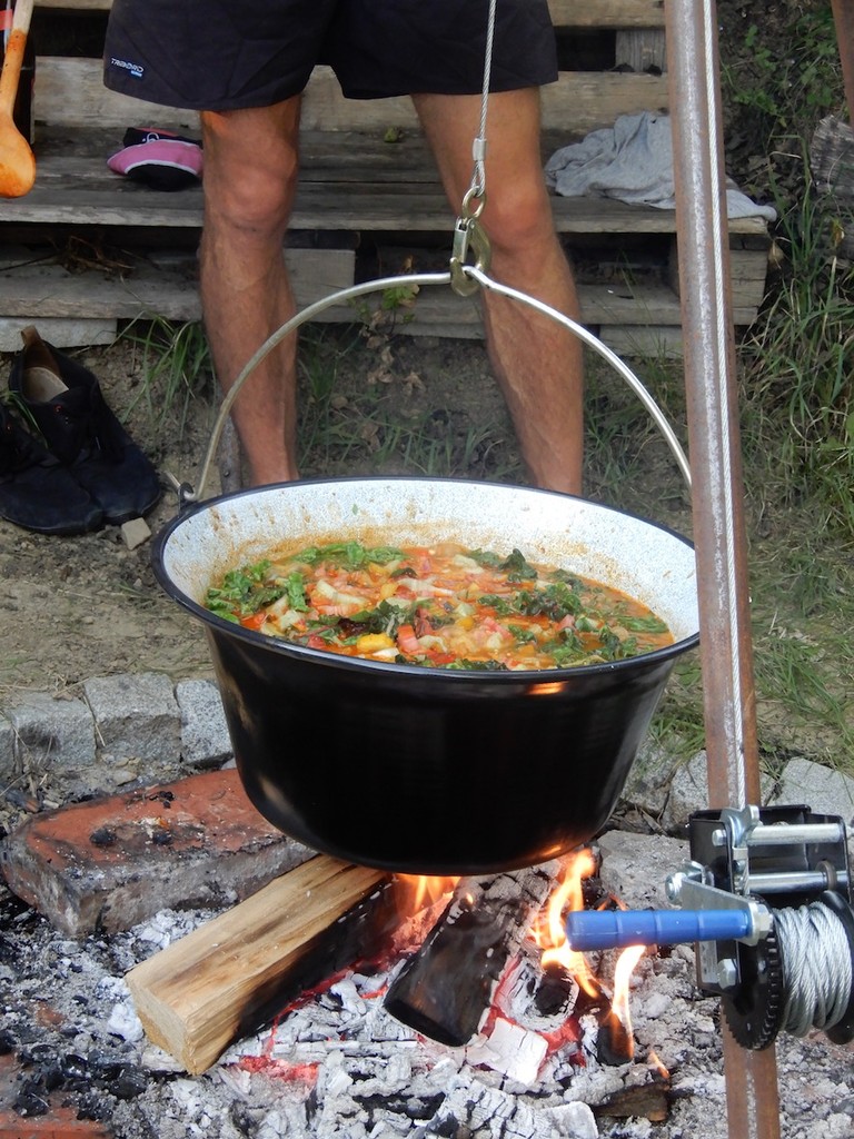 Buntes Gemüse kocht in einem Kessel, der über einer offenen Feuerstelle hängt