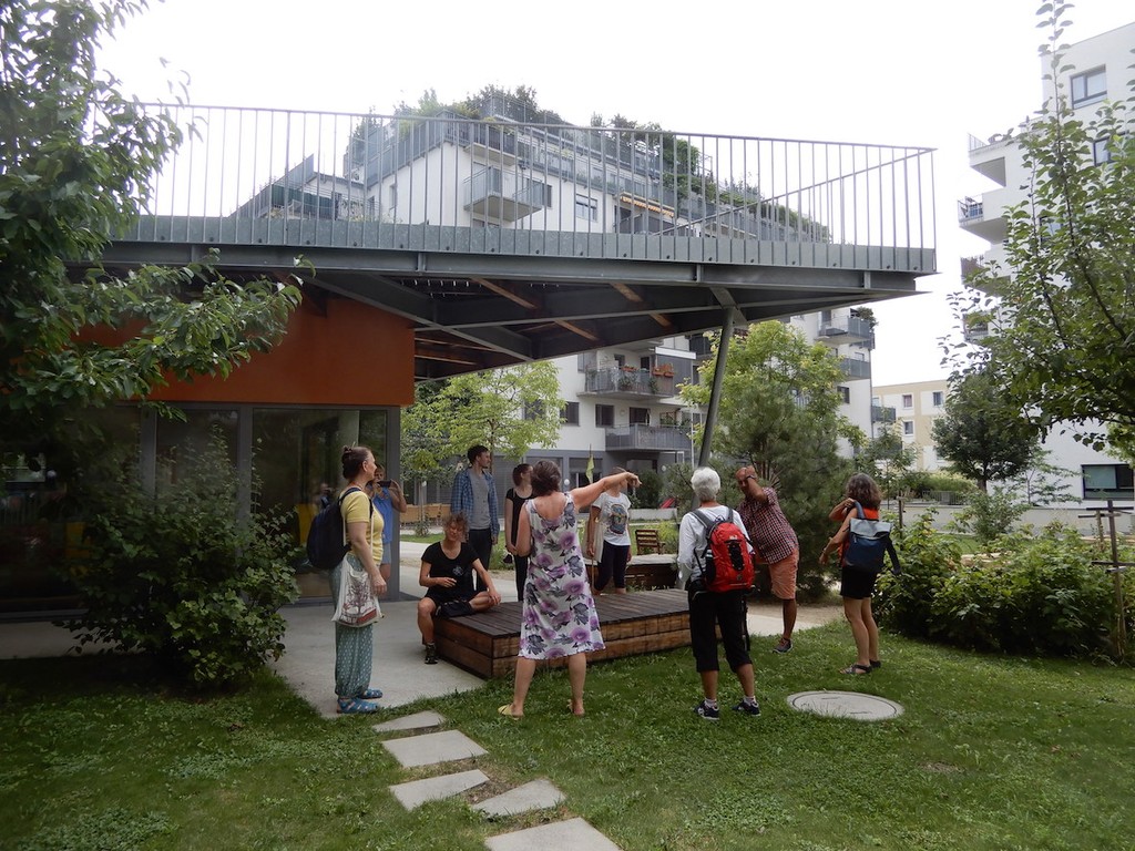 Menschengruppe steht und sitzt in einem grünen Garten unterhalb eines Balkons